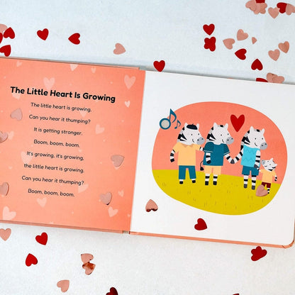 
An open children's book spread on a white background with scattered red and pink hearts. The left page has the title 'The Little Heart Is Growing' and a poem on a peach background.