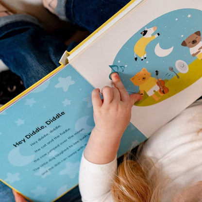 
A young child's hand pressing a musical button on an open "Hey Diddle, Diddle" nursery rhyme book.