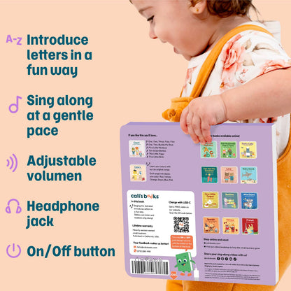 
A child wearing orange bibs holds a Call's Books interactive reading board. The back of the board is light purple with product features listed on the left, including letters, singing, adjustable volume, headphone jack, and on/off button.