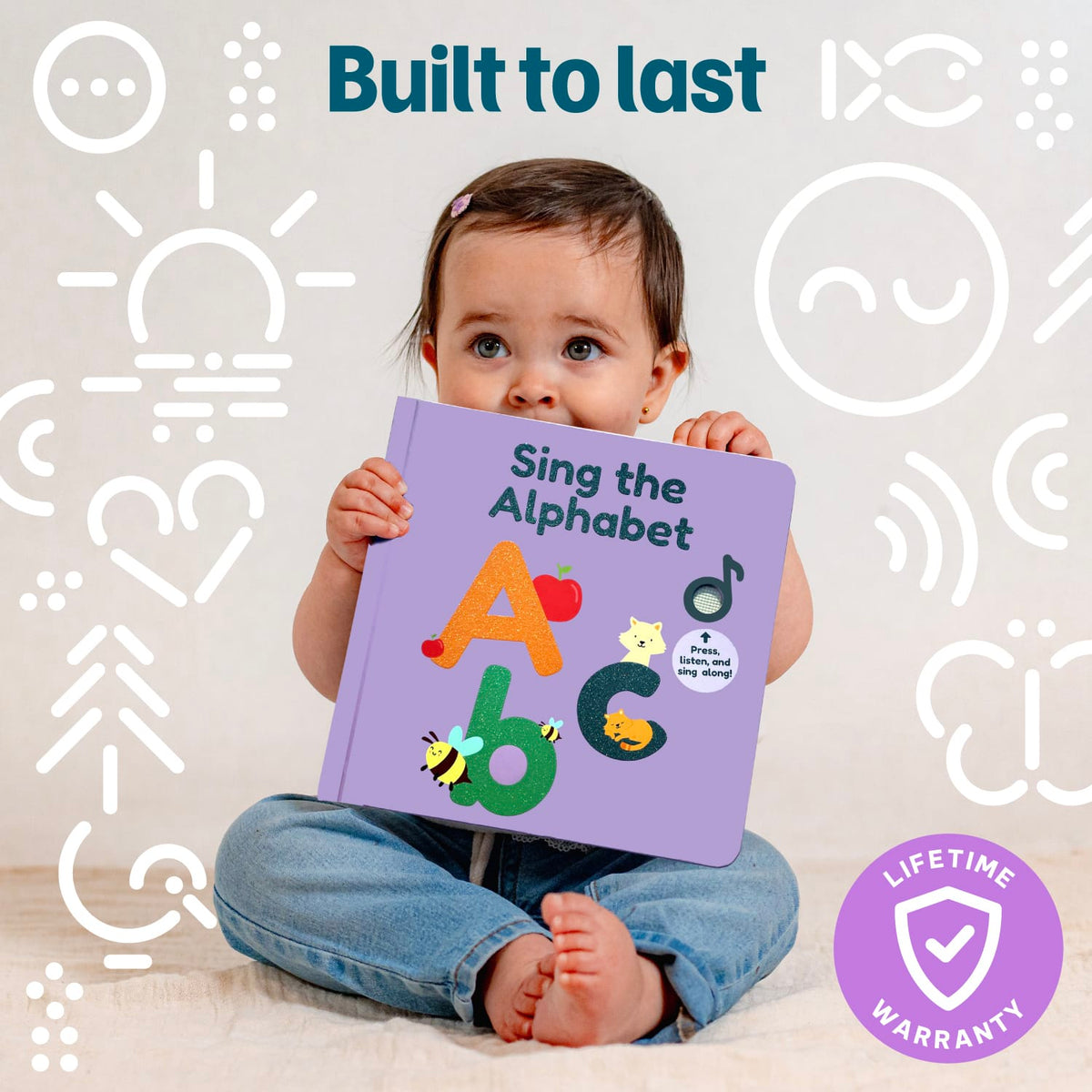 
A baby sitting on a light floor holding a purple children's alphabet book titled 'Sing the Alphabet.' The background is white with simple white line icons, and the image includes the text 'Built to last' and a purple 'Lifetime Warranty' badge.