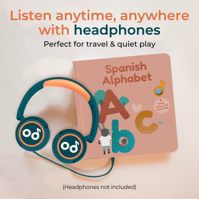 
A children's Spanish Alphabet book with colorful illustrated letters is shown next to teal and orange over-ear headphones on a light background. Large text at the top reads 'Listen anytime, anywhere with headphones' and 'Perfect for travel & quiet play,' with smaller text below and a note at the bottom saying '(Headphones not included)'.