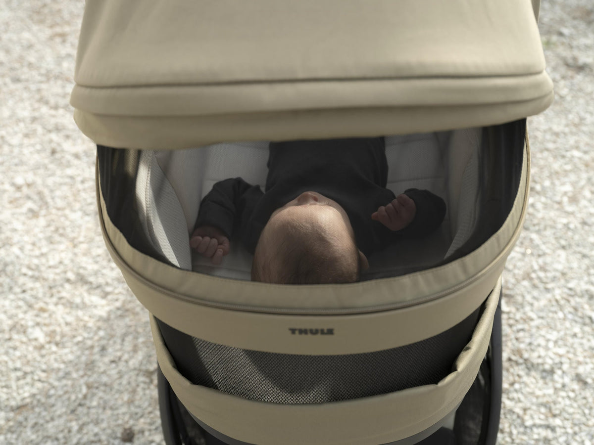 Close-up of a newborn sleeping in the Thule Charm stroller's carrycot bassinet.
