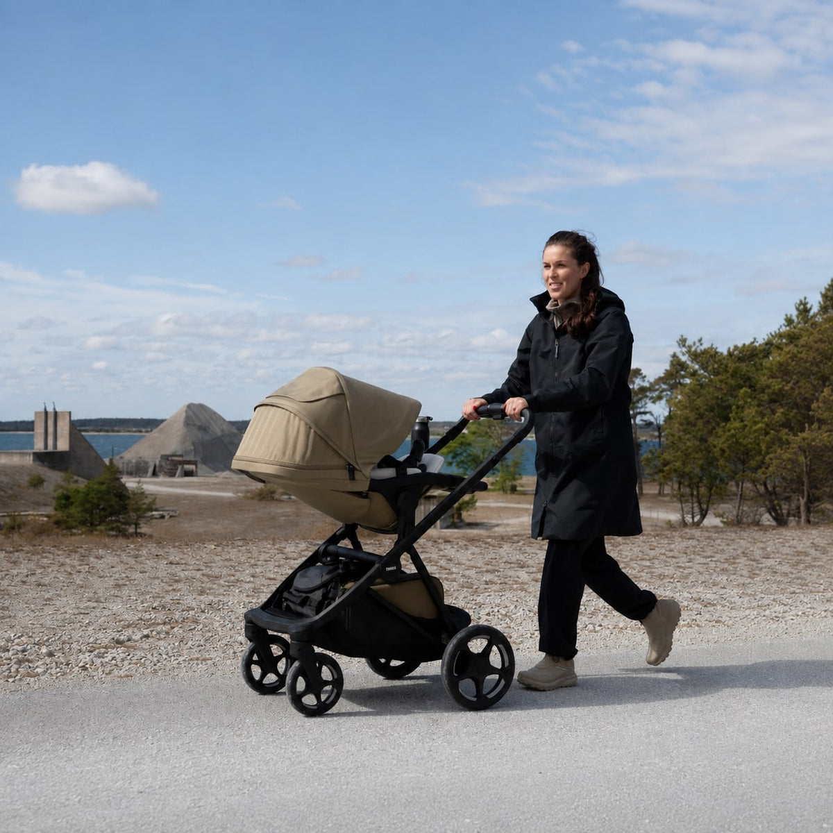 A woman walks with the Thule Charm stroller along a coastal path.

