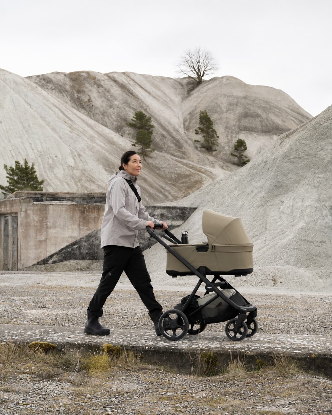 Woman pushing the Thule Charm 2-in-1 stroller in bassinet mode on a gravel path through a quarry landscape.
